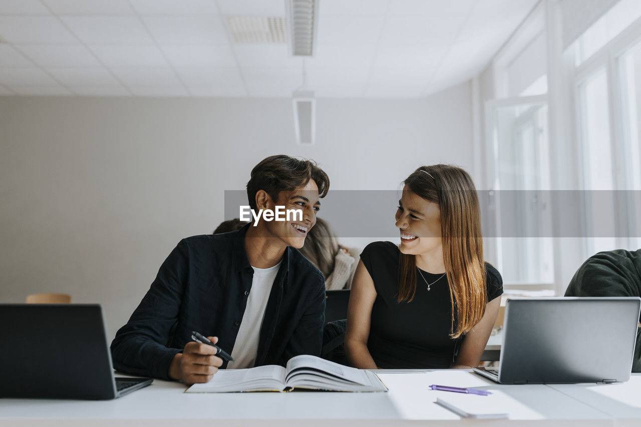 Happy male and female students studying together in classroom