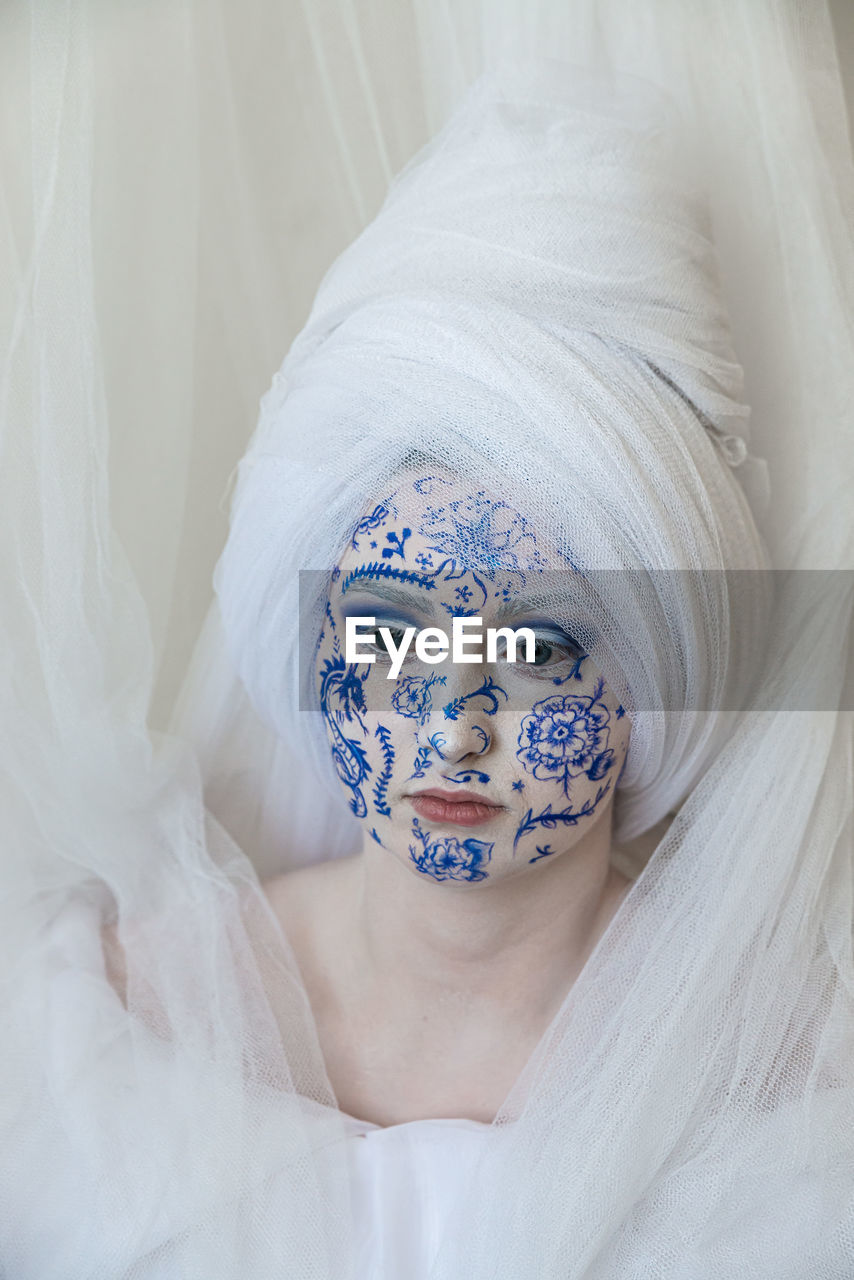 Woman with painted face looking away against curtain at home