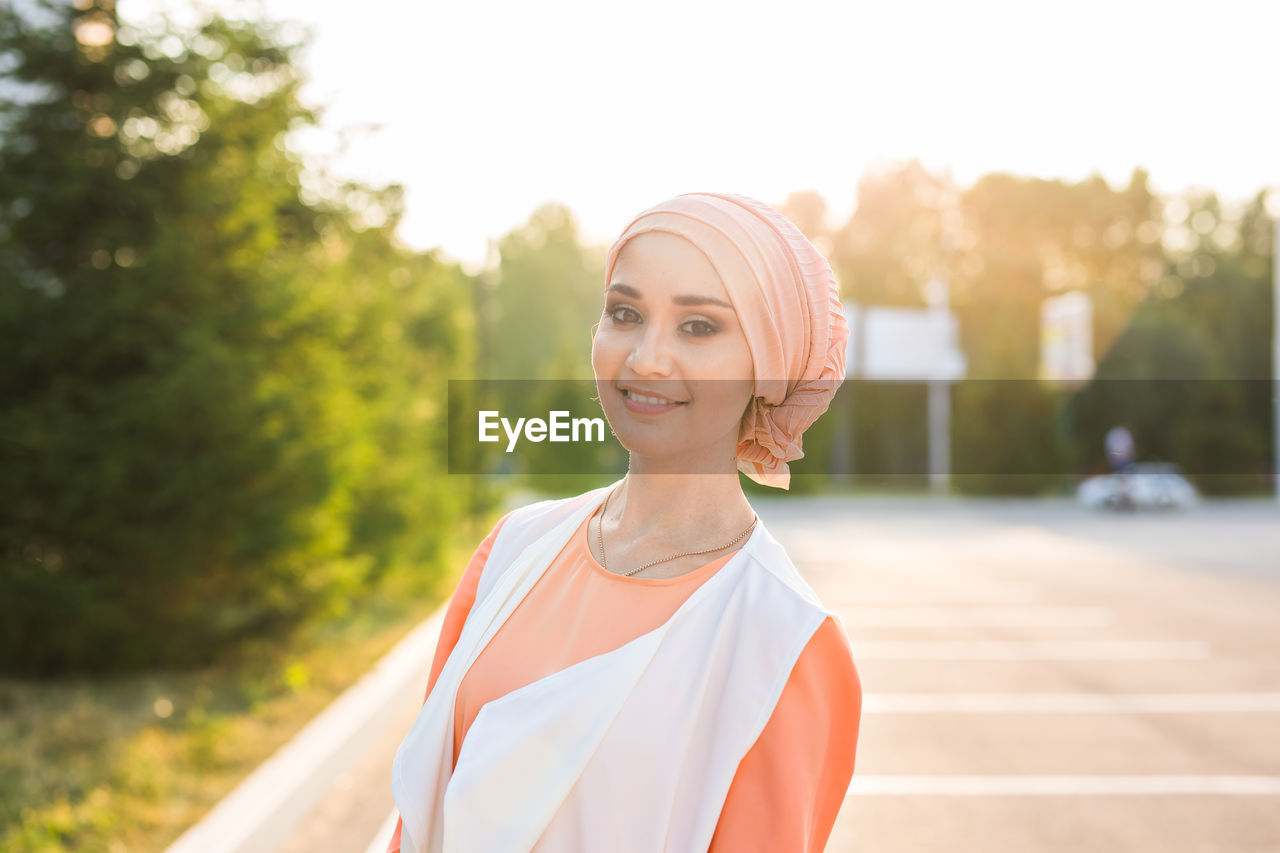 PORTRAIT OF SMILING WOMAN STANDING OUTDOORS