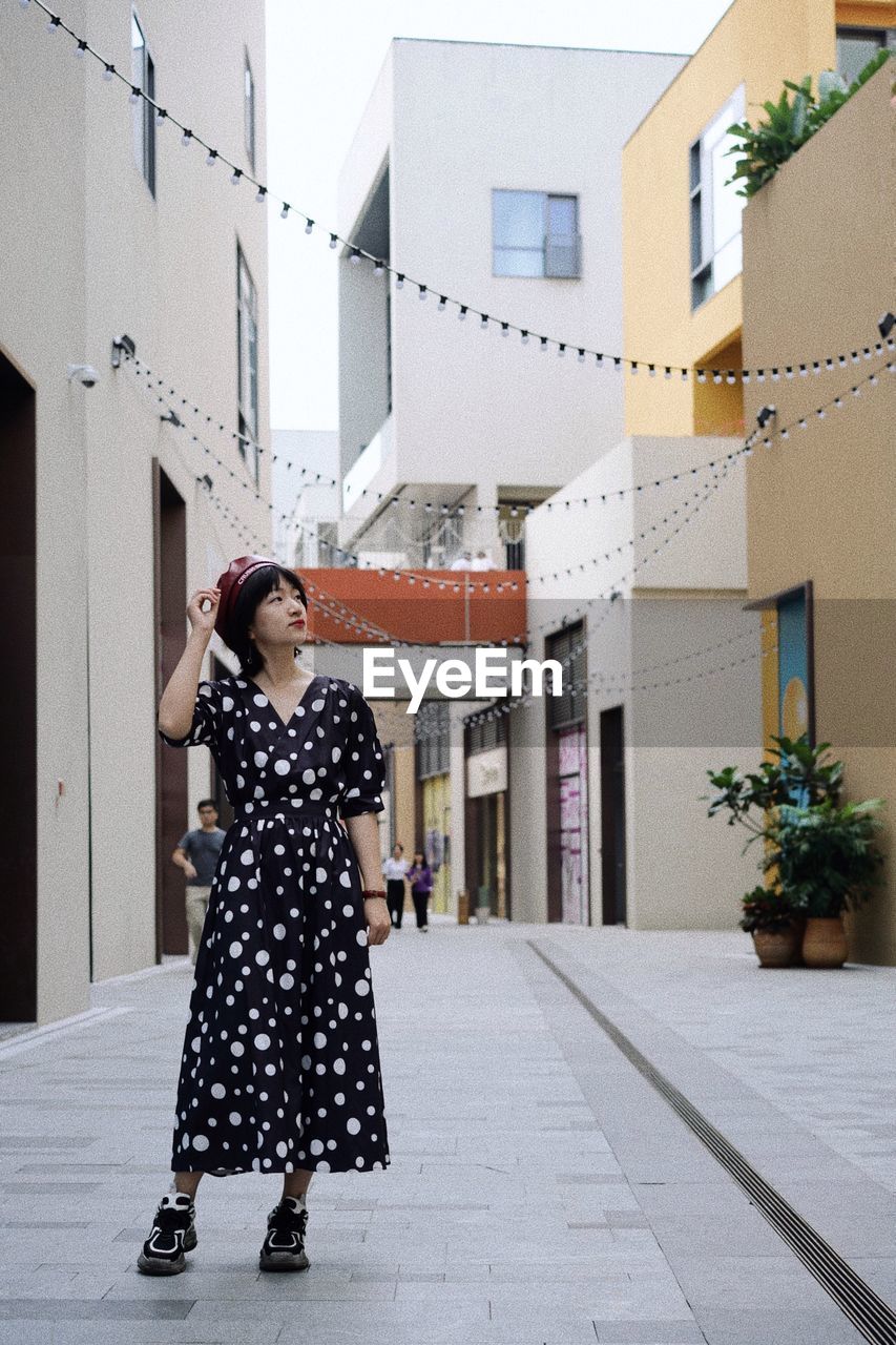 Woman standing on footpath amidst buildings in city