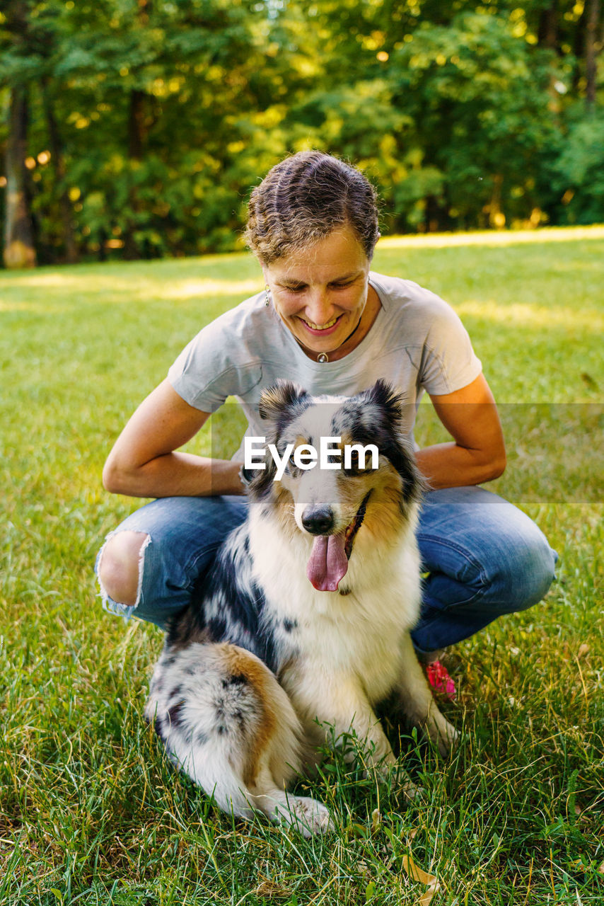 Happy young woman spending time with lovely spotted australian shepherd dog in green meadow on