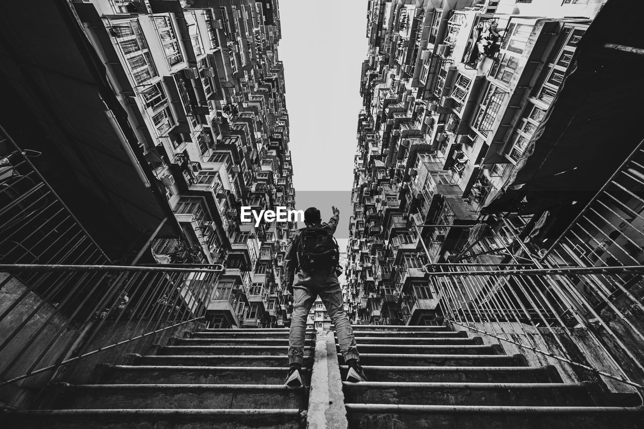 REAR VIEW OF MAN WALKING ON STAIRCASE AMIDST BUILDINGS