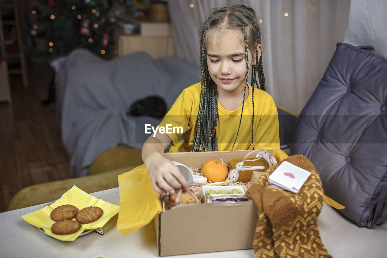 Girl packing care box with tea, honey, cookies and knitted wool socks for grandmother on christmas