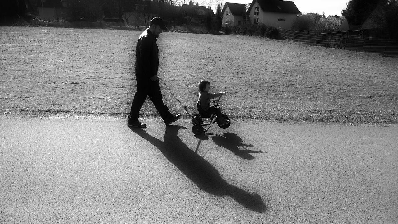 Father assisting son in riding tricycle on street