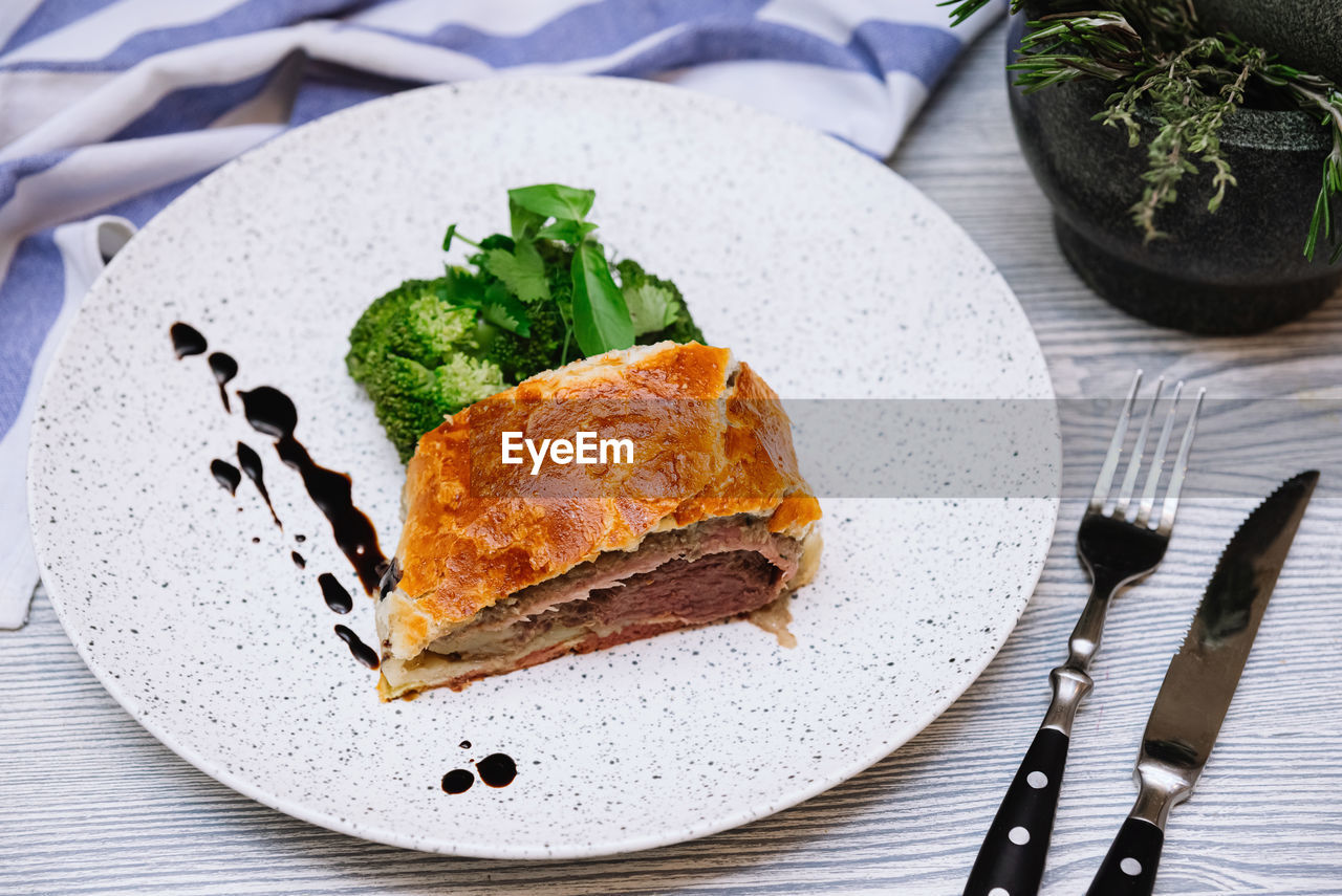 Slice of beef wellington with steamed broccoli dressed with the thick balsamic sauce drops
