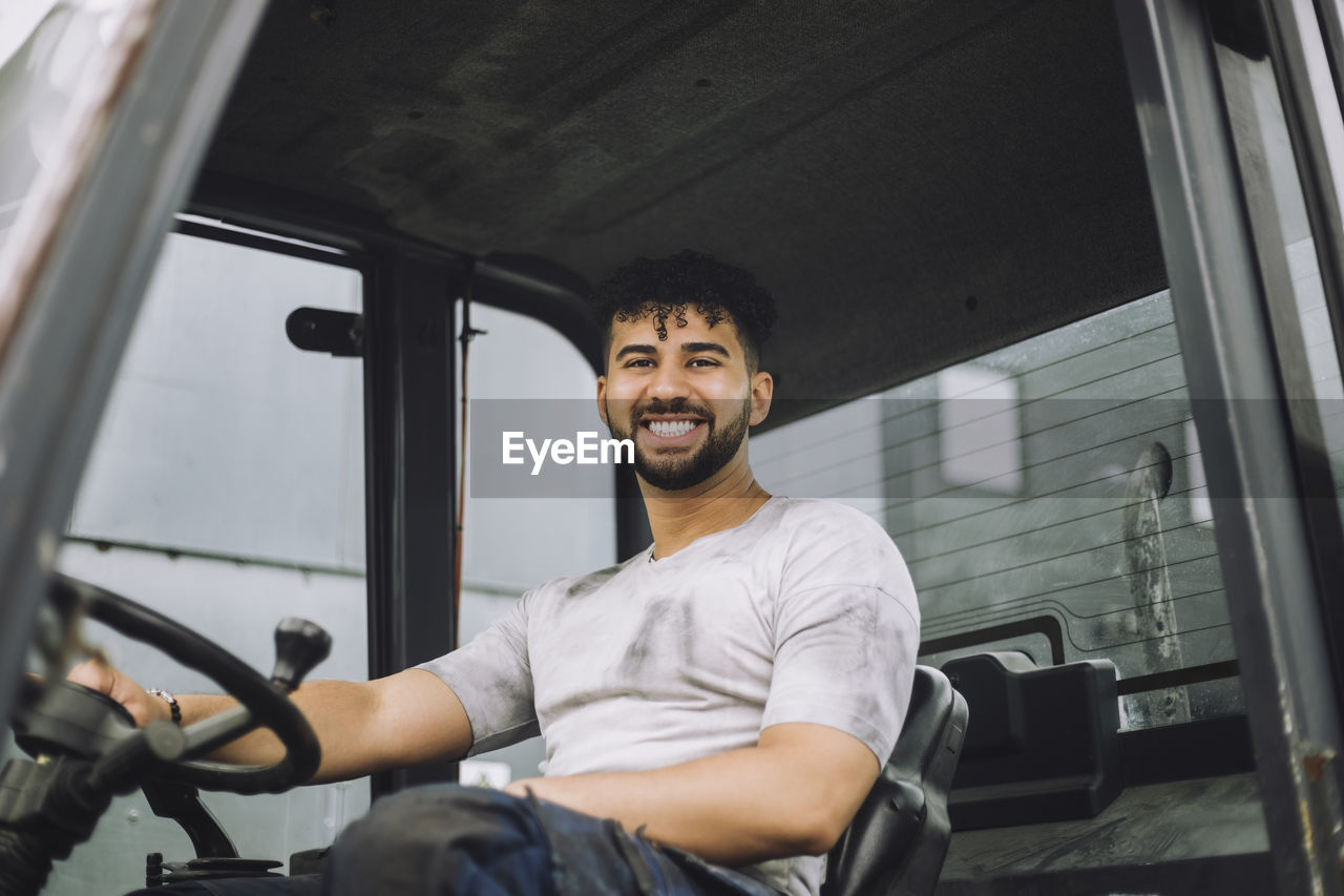 Portrait of happy young construction worker sitting in vehicle