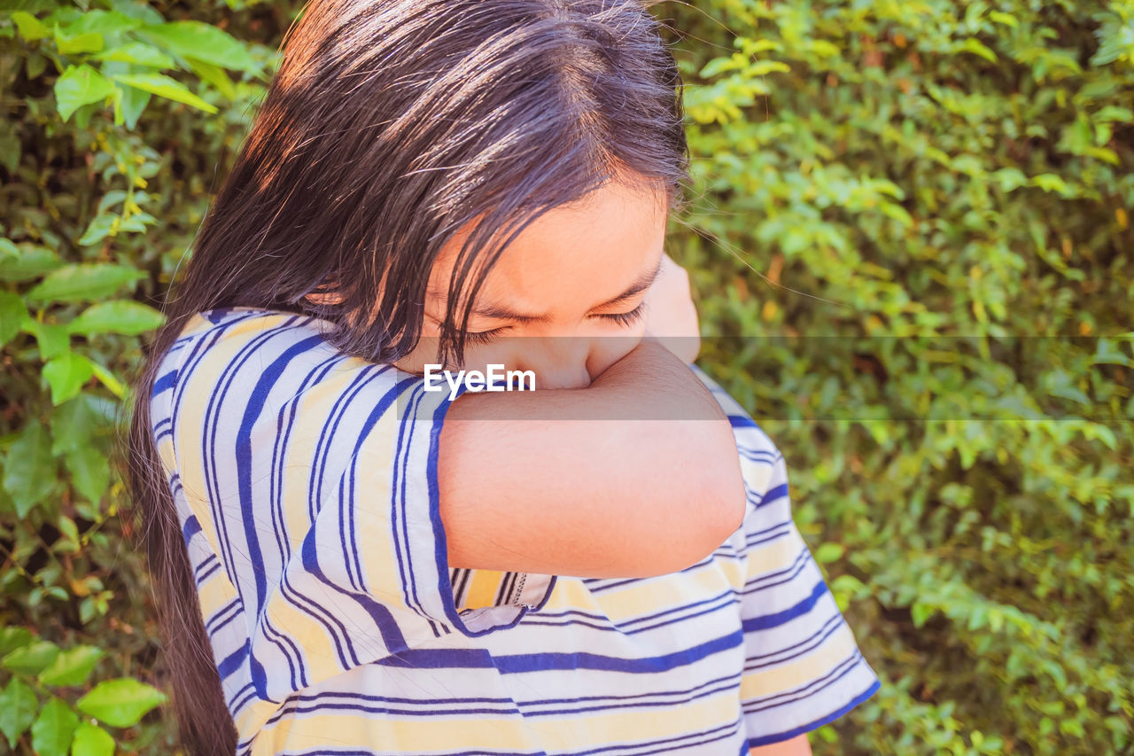 Coronavirus concept, asian child girl sneezing on hinge joints arm outdoor for protect