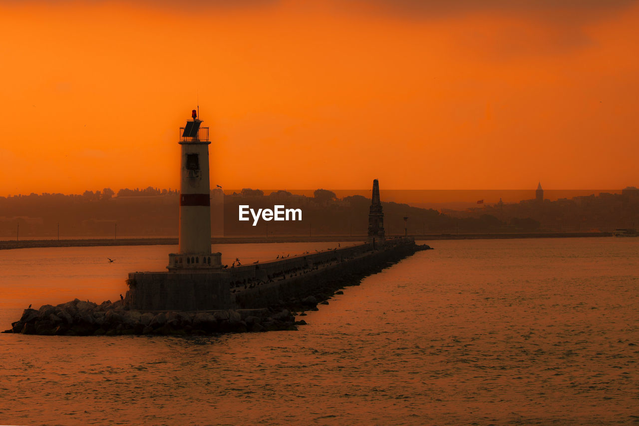 Calm sea with lighthouse in distance against clear sky