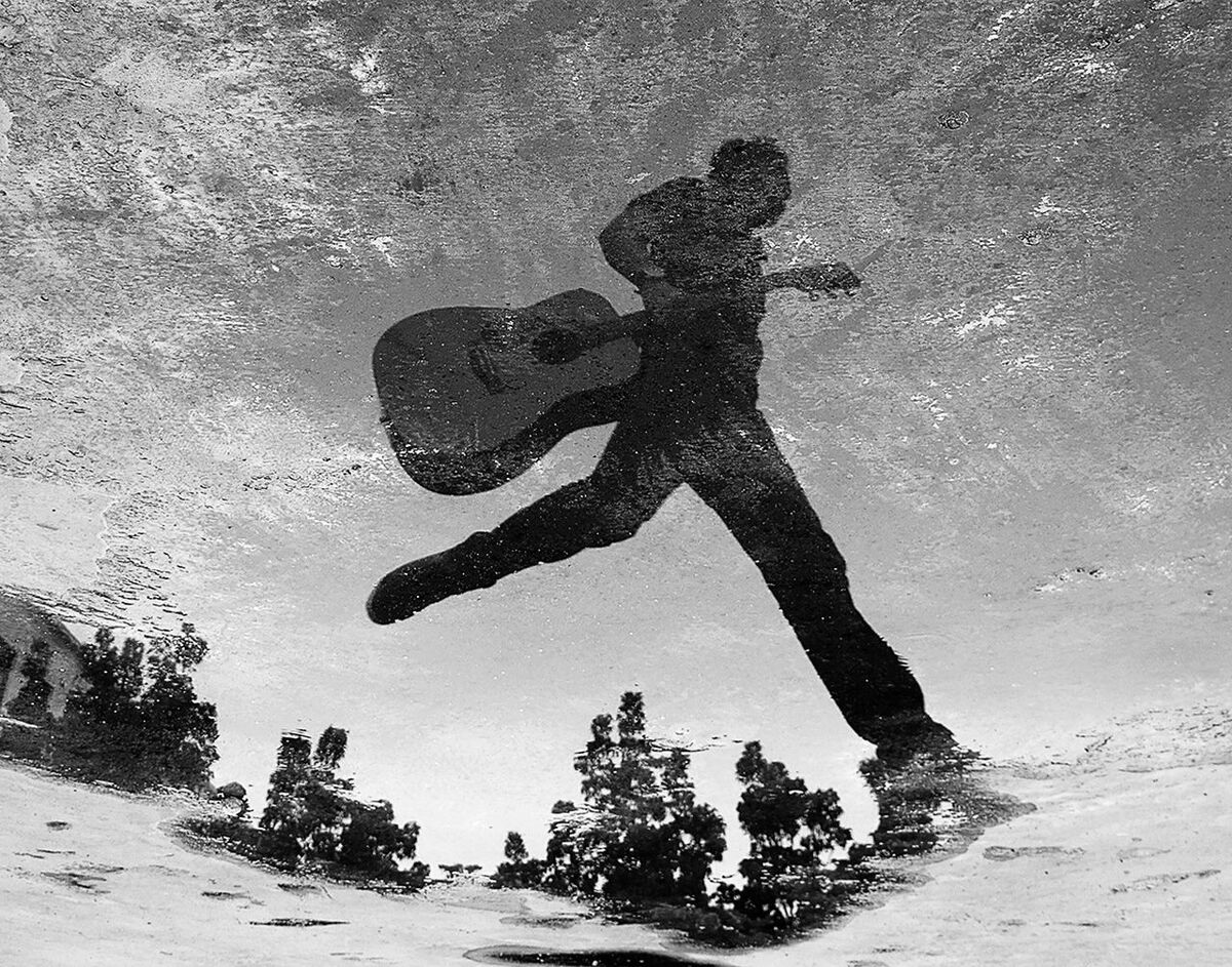 Reflection of man walking in puddle on street