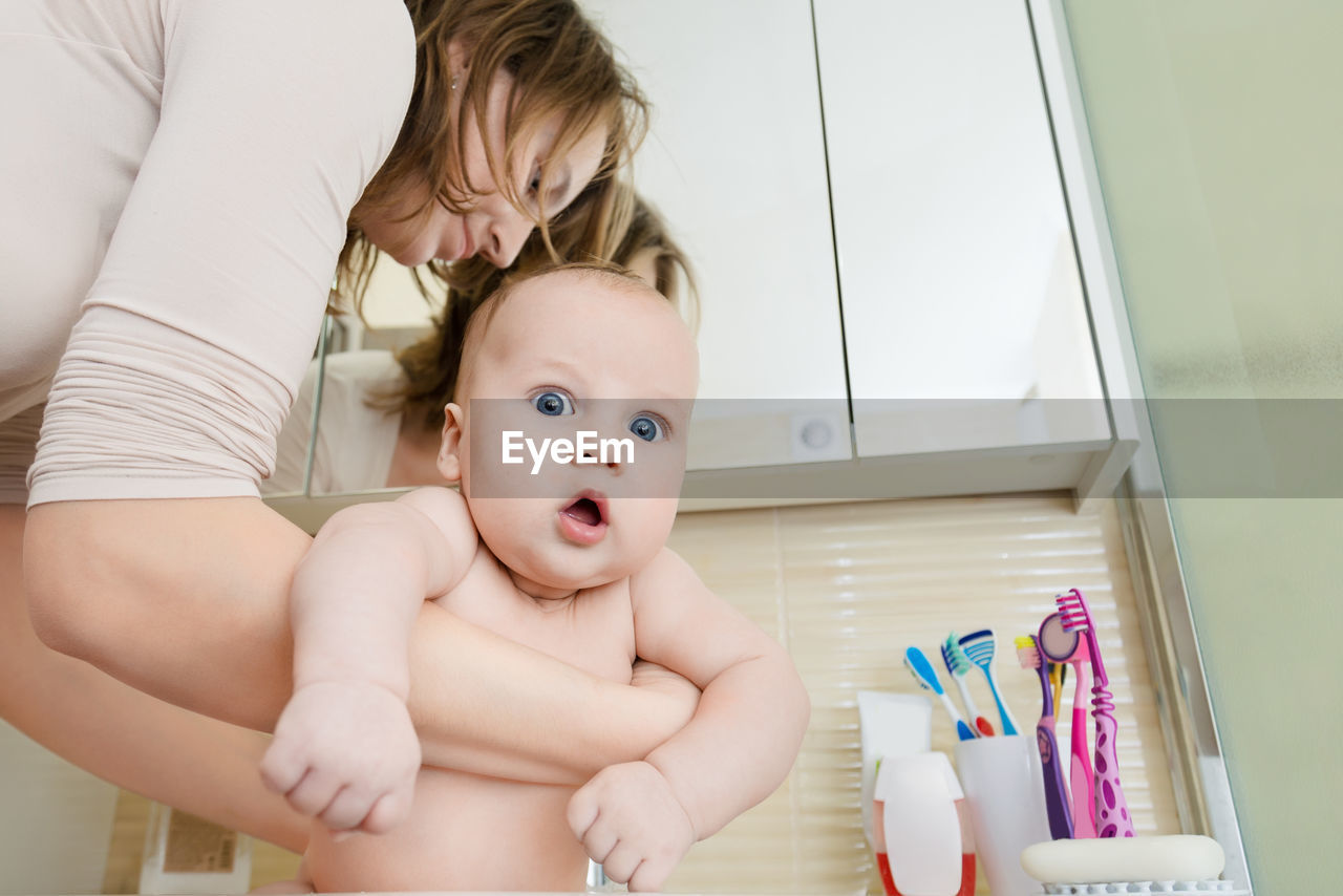 Low angle view of mother carrying shirtless son in bathroom at home