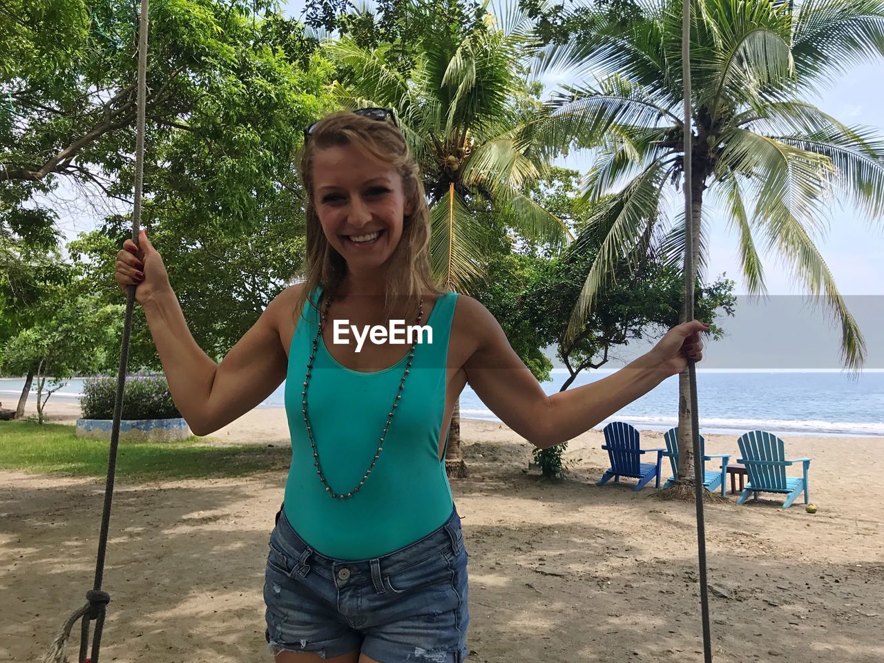 Portrait of smiling woman standing on swing at beach