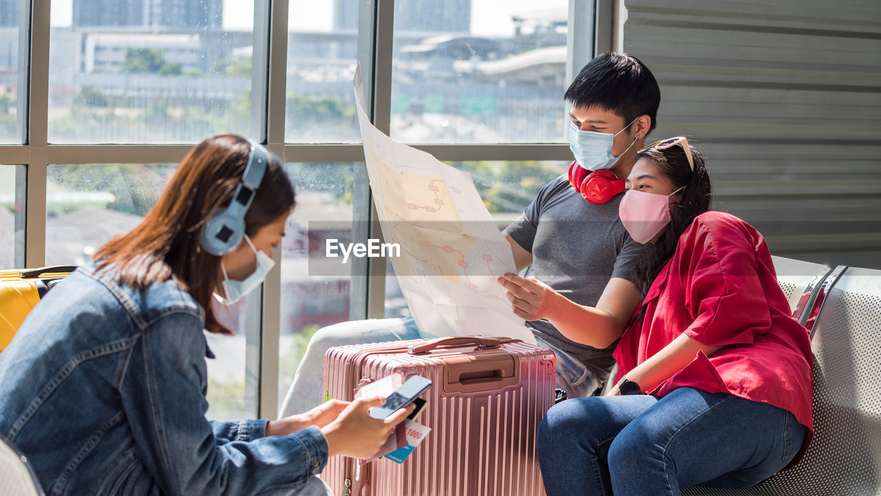 Couple wearing mask looking at map while sitting at airport