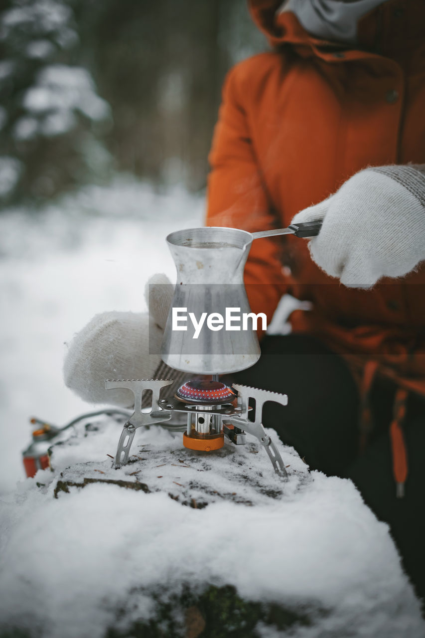 Midsection of woman making drink on camping stove during winter