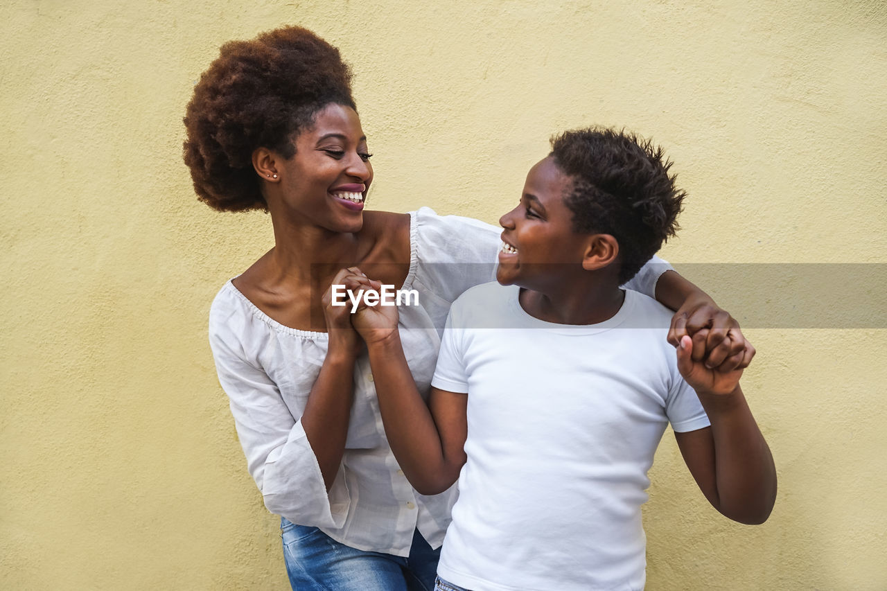 Smiling siblings standing against wall