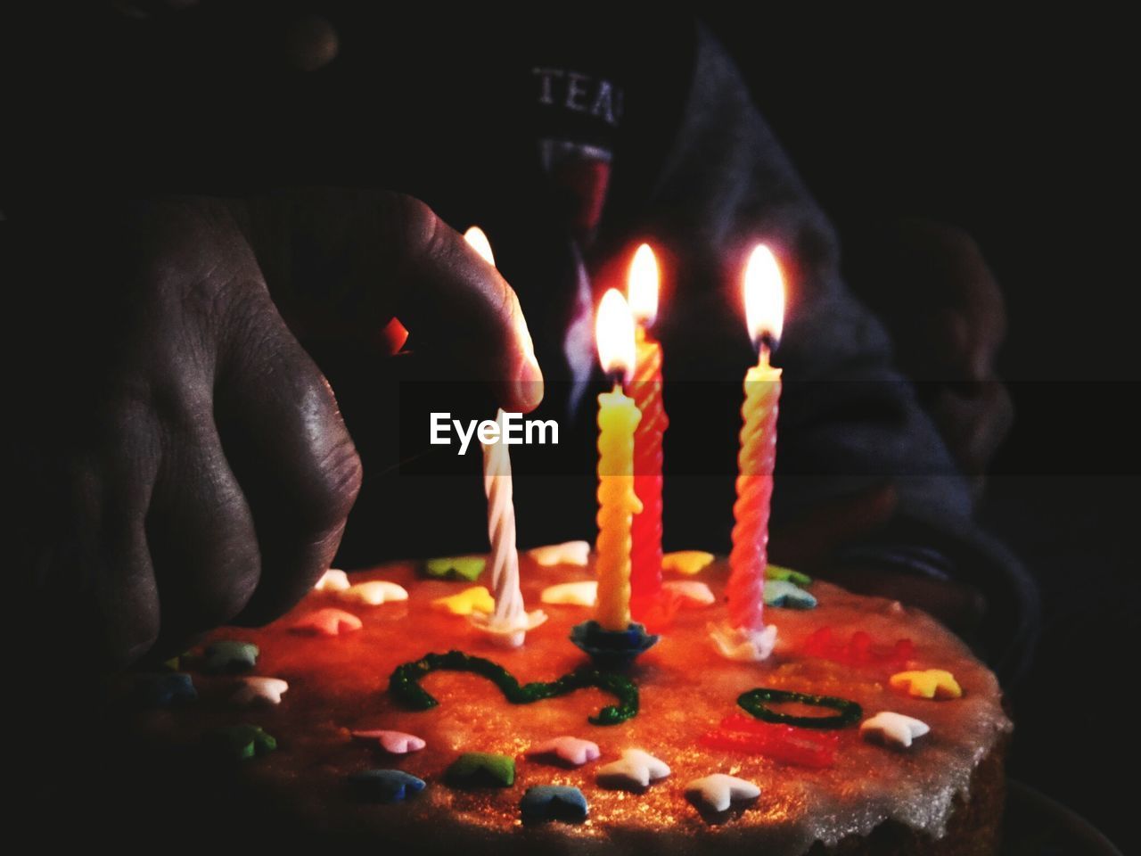 Cropped hand of person holding lit candles on cake