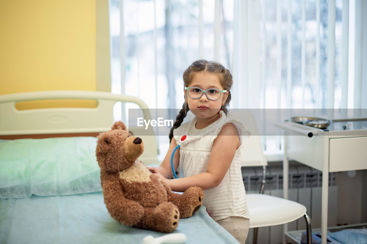 A girl in a hospital room plays doctor with a teddy bear. fun for the child while in the hospital