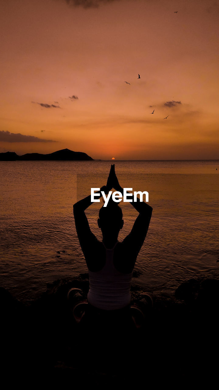 Rear view of woman standing at beach against sky during sunset