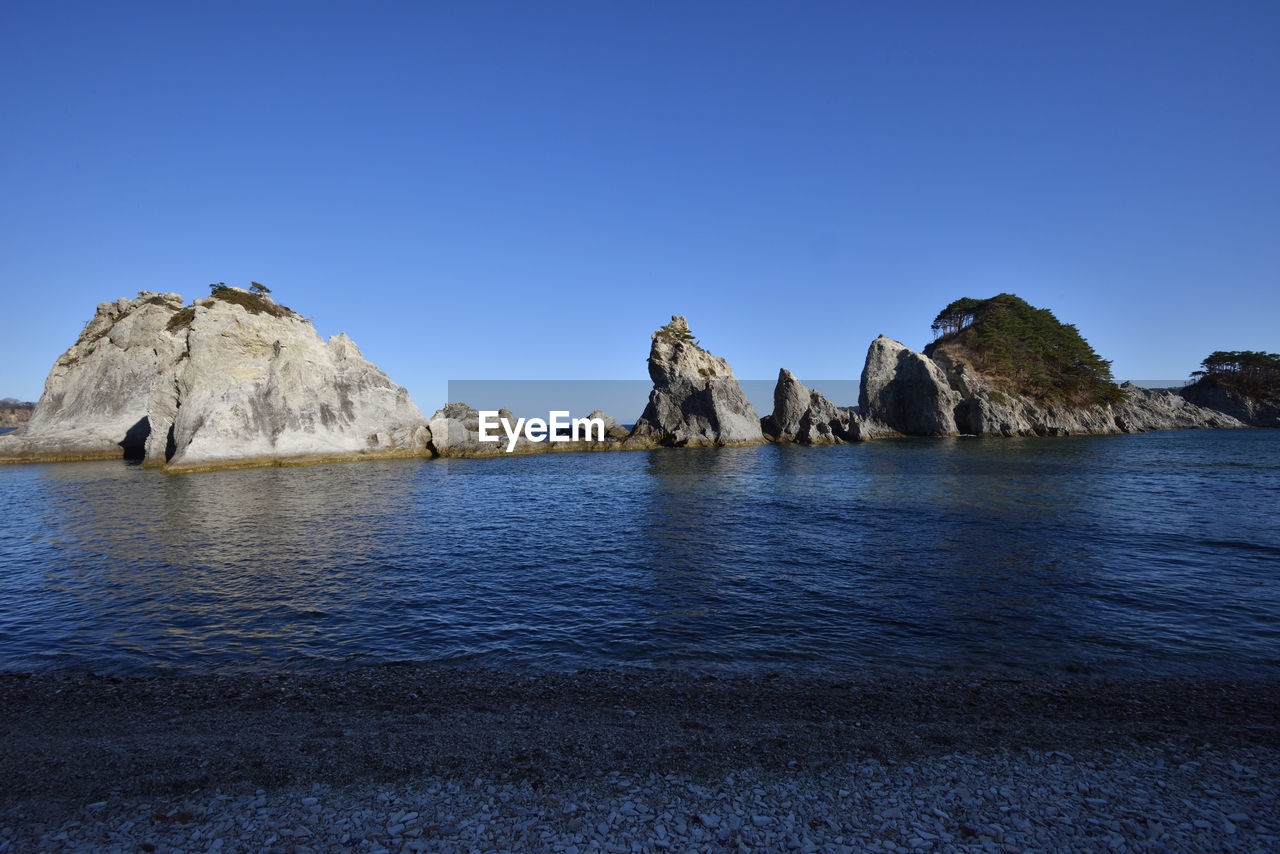 Scenic view of rocks in sea against clear blue sky