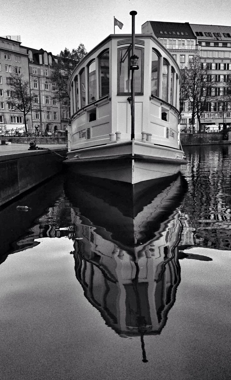 Reflection of moored ferry boat in sea against buildings