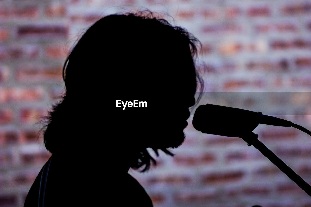 Side view of silhouette singer by microphone against brick wall