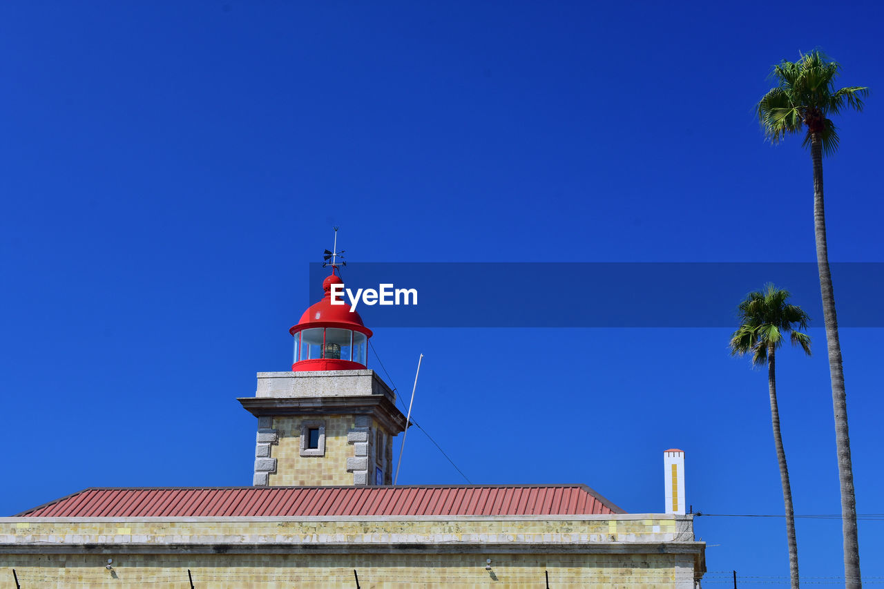 Low angle view of lighthouse by building against clear blue sky