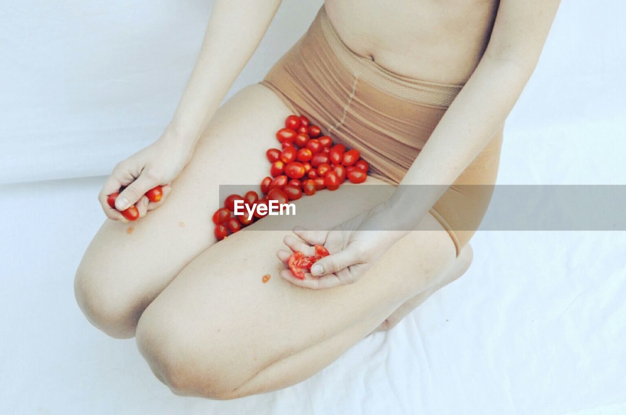 Low section of woman with fruits sitting on bed
