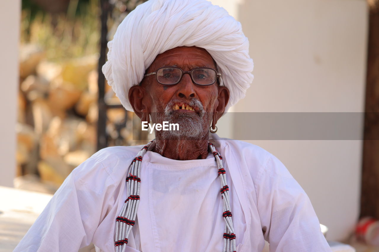 Portrait of a old aged man with his white big round cap and silver color chain , indian culture.