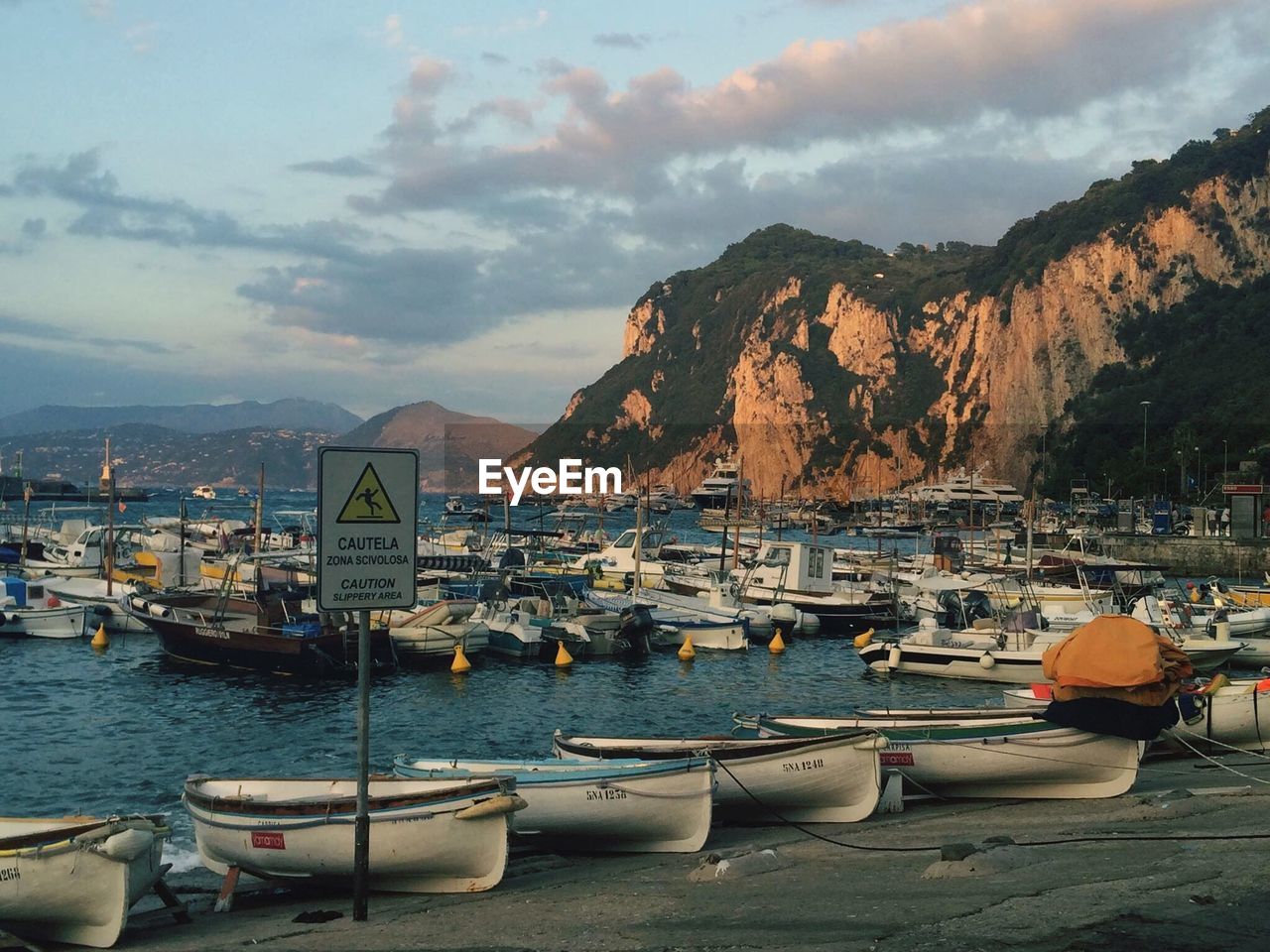 Boats moored on sea by mountain against sky