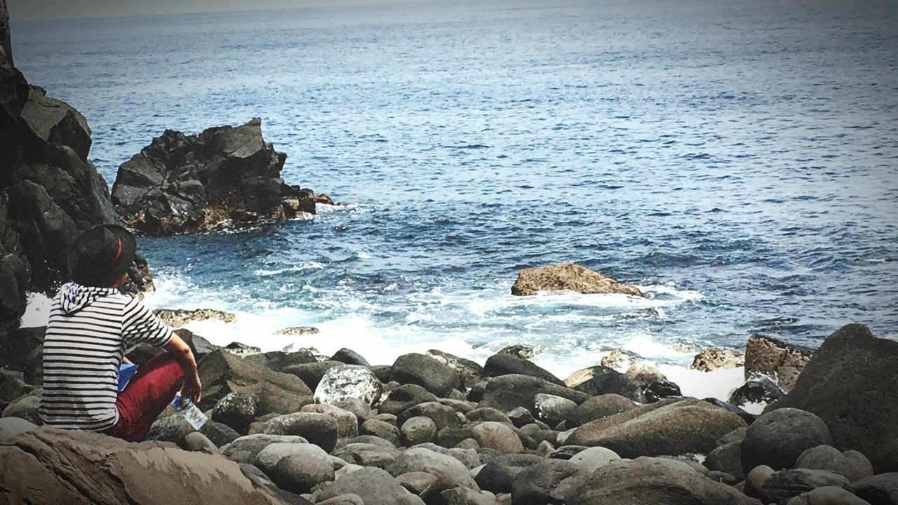 Rear view of man sitting on rocks at beach