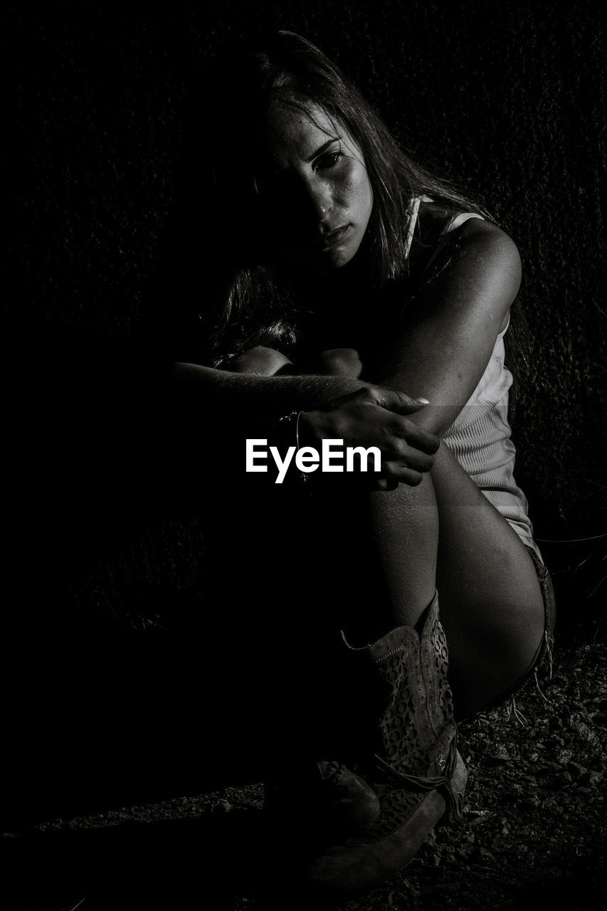 Woman hugging knees while sitting on field at night