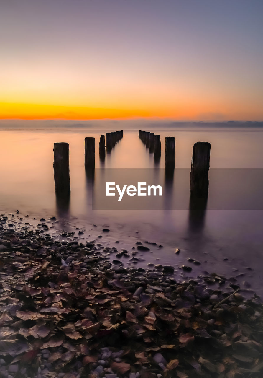 WOODEN POSTS IN SEA AT SUNSET