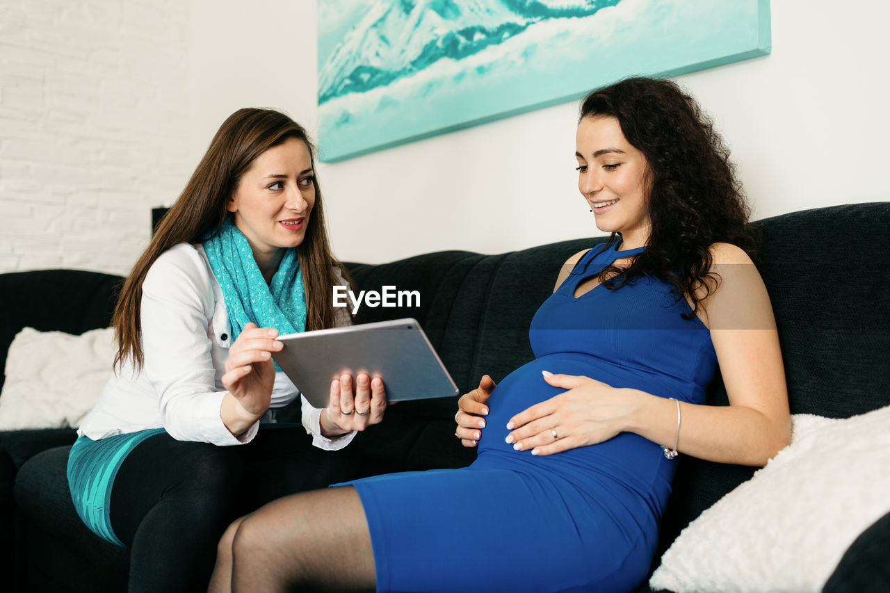 Pregnant woman with doctor using digital tablet while sitting in hospital