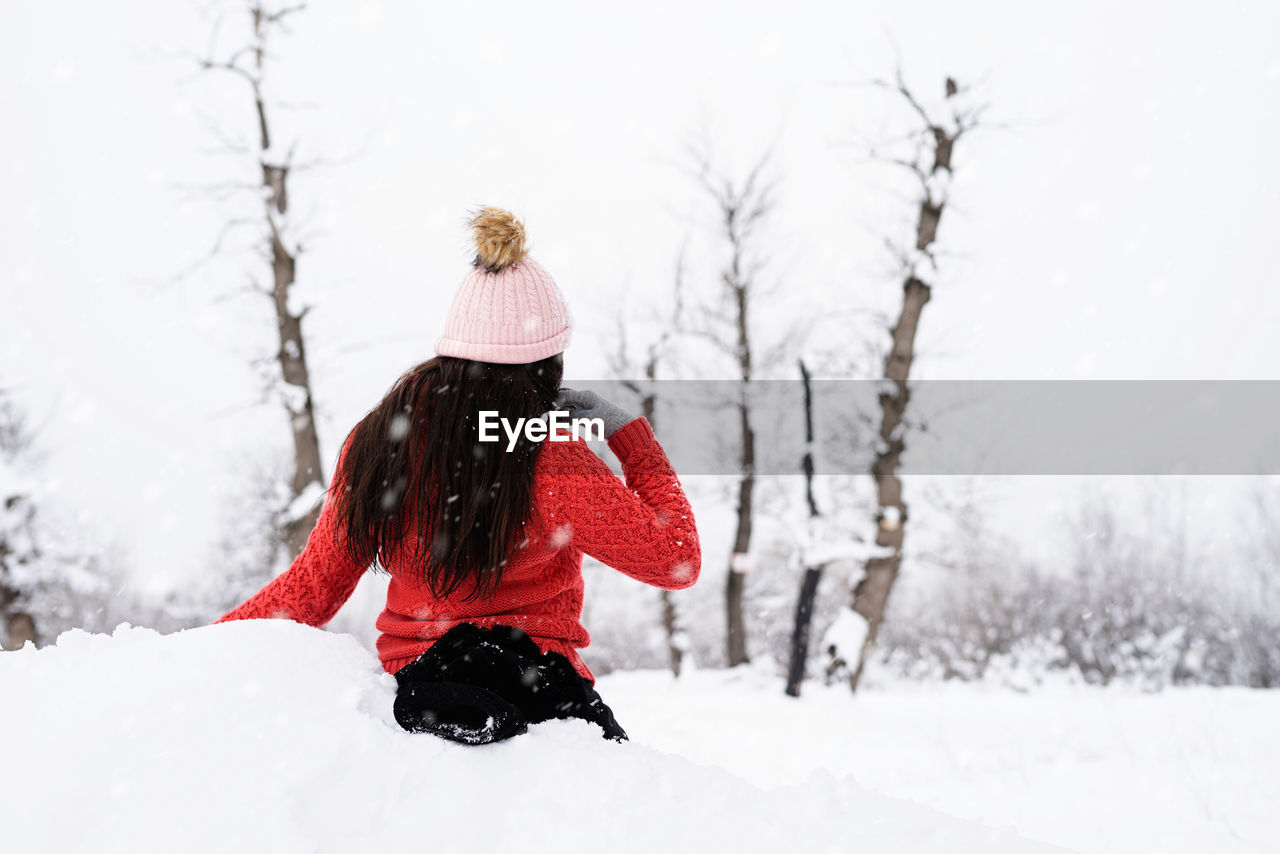 Winter season. portrait of a beautiful smiling woman in red sweater and hat in snowy park