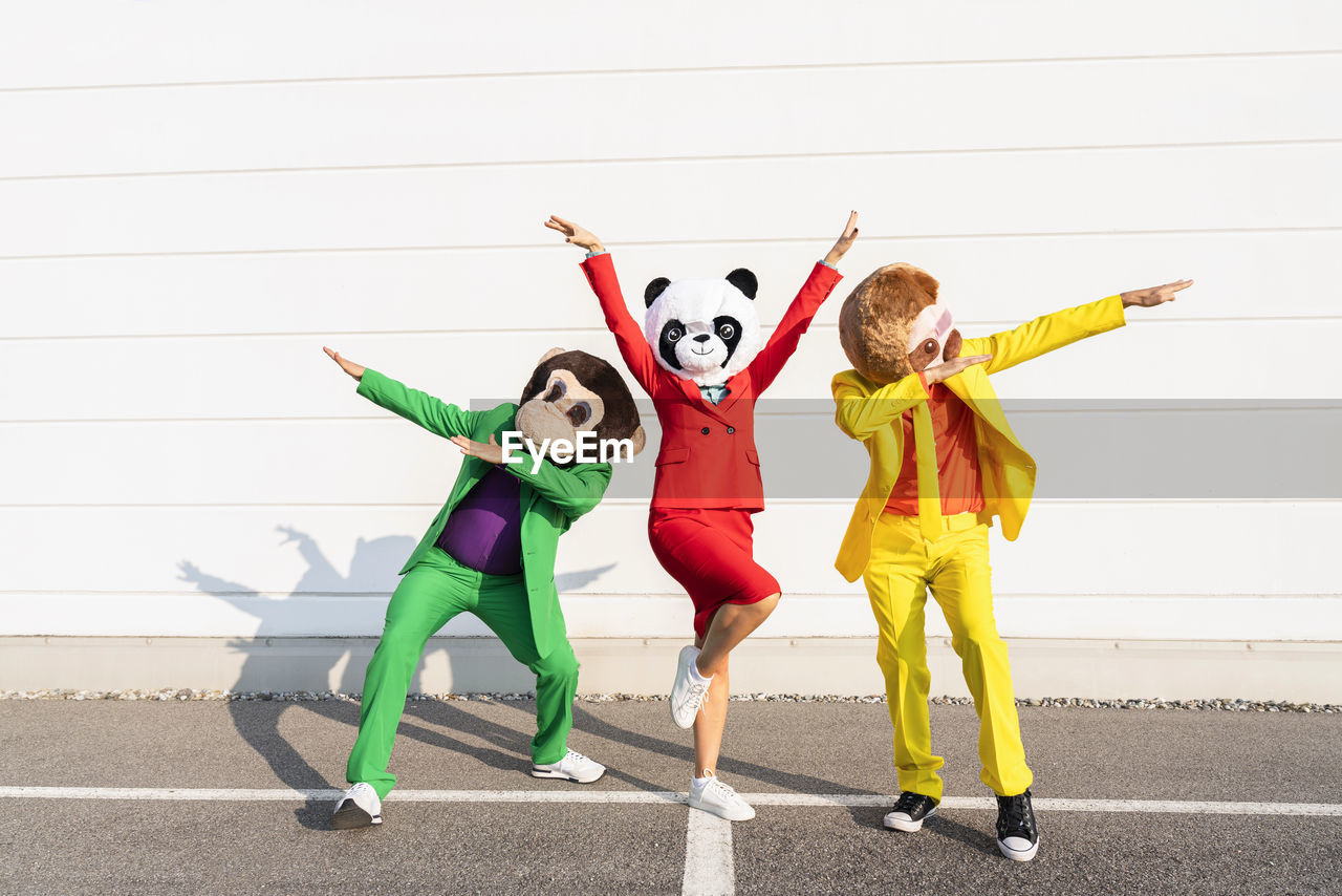 Playful friends wearing animal mask and dancing in front of wall