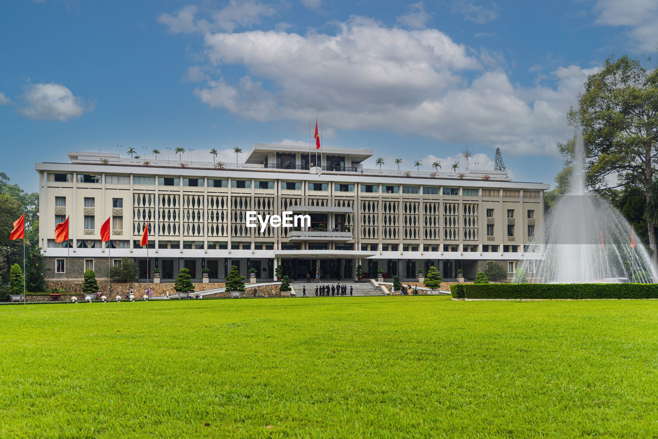 architecture, grass, built structure, building exterior, sky, travel destinations, government, plant, nature, flag, city, travel, palace, landmark, cloud, tourism, the past, history, politics and government, building, politics, estate, lawn, day, outdoors, château, facade, fountain, tree, green, environment, authority, mansion, sport venue, no people, architectural column