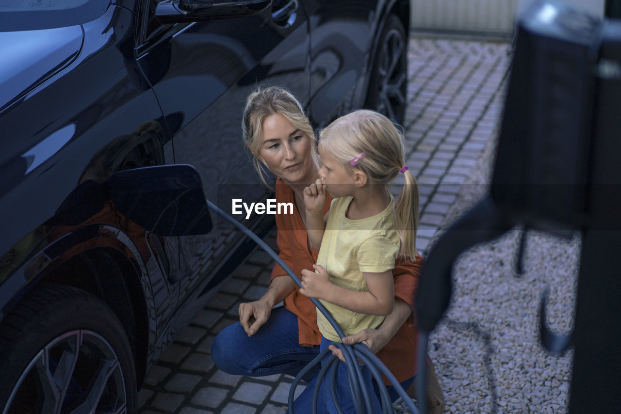 Girl with mother charging electric vehicle in front yard