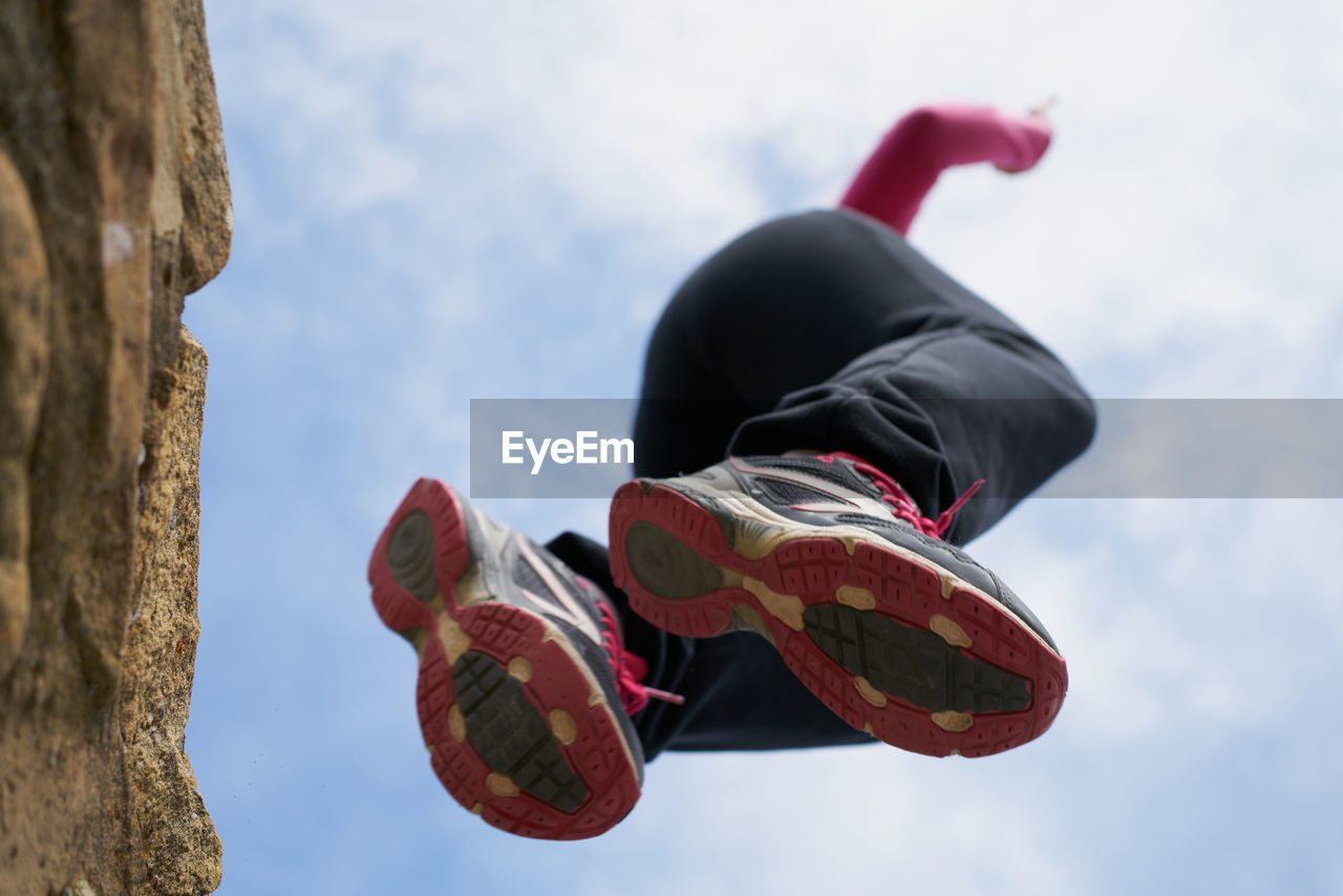 From below female in sneakers jumping from rough stone wall