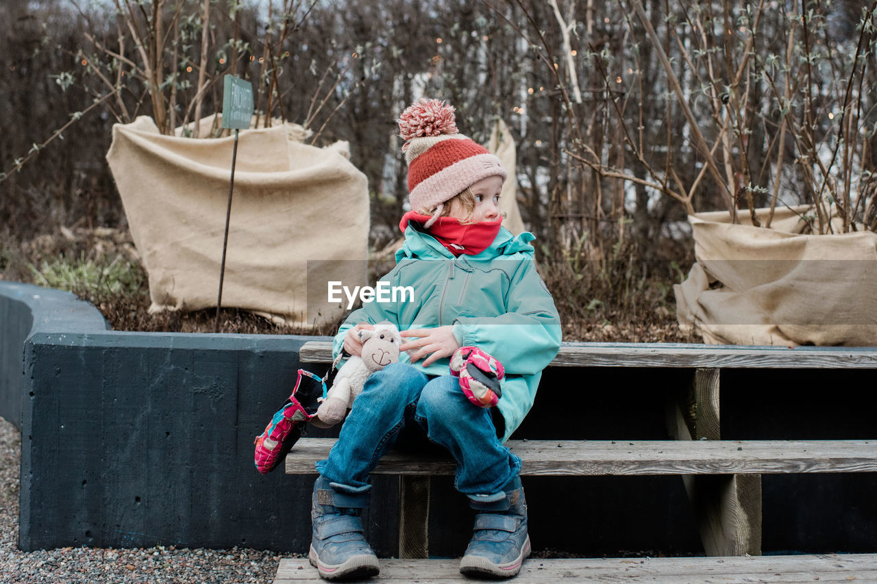 Young girl wrapped up warm sitting with her toys in a garden in winter