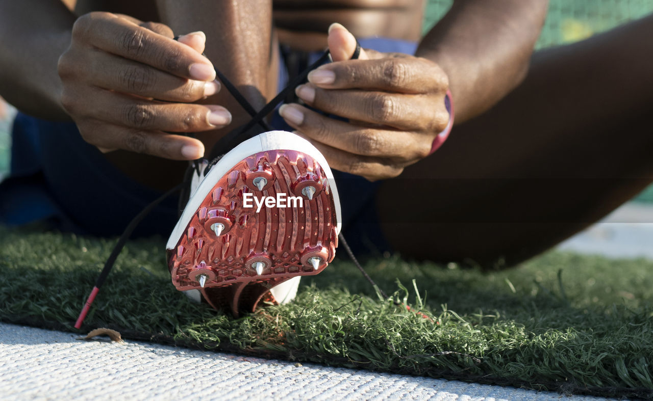 Sportswoman tying shoelace of spikes running shoes in sports court