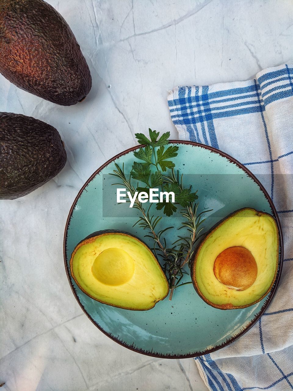 Fresh avocado with herbs and lemons lies on the table on blue plate on white background. flat lay