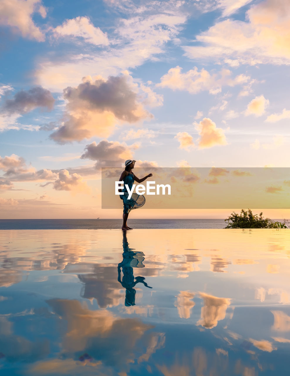 rear view of man with arms outstretched standing at beach against sky during sunset