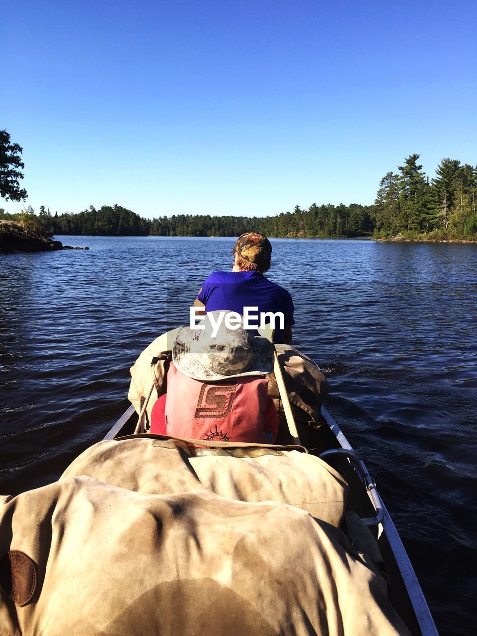 Rear view of man sitting in boat on lake against clear sky