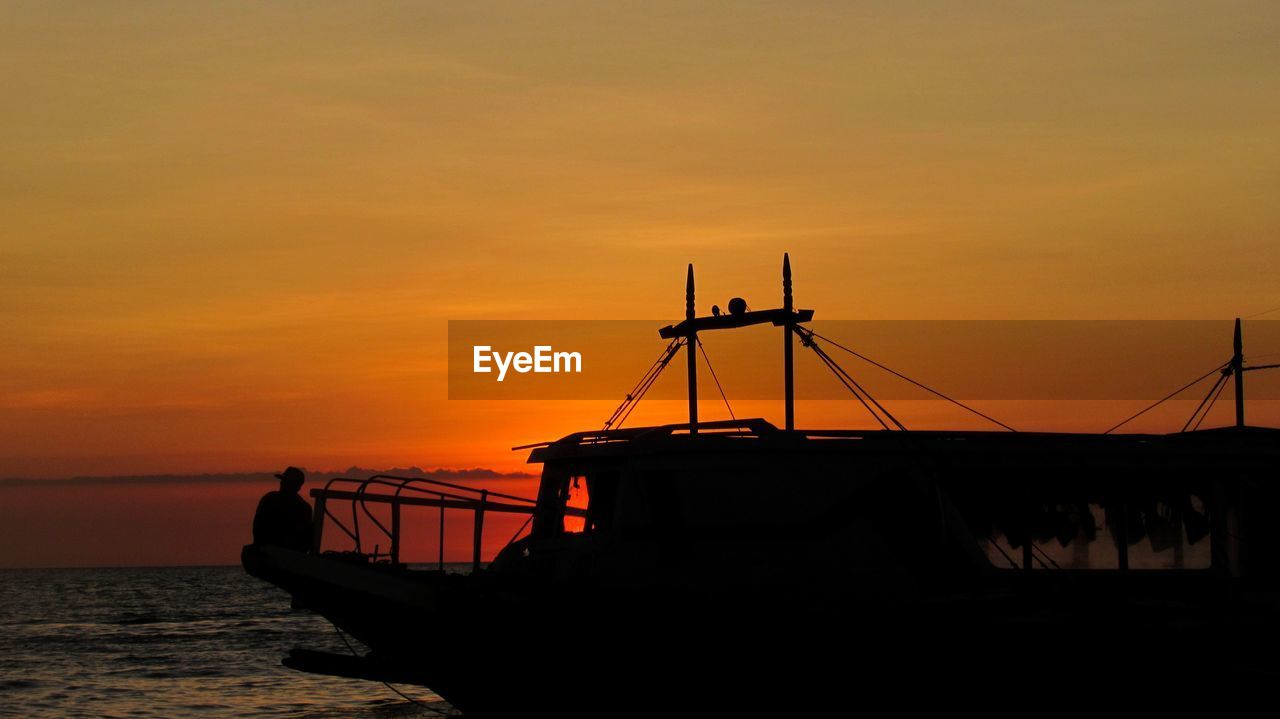 Silhouette boat moored on sea against orange sky