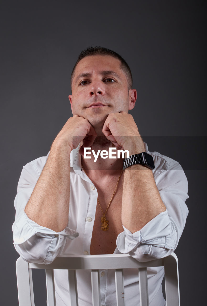 studio shot, one person, adult, portrait, men, indoors, person, front view, arm, black background, clothing, looking at camera, emotion, hand, gray, looking, gray background, waist up, sitting, mature adult, serious, cut out, contemplation