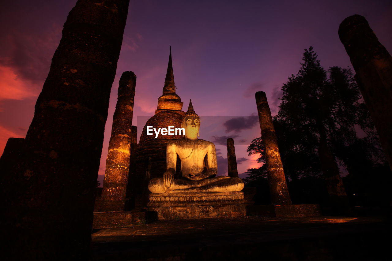 Low angle view of buddha statue and temple against sky at night