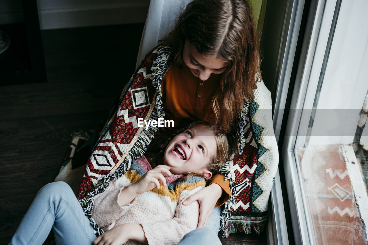 Playful girl laughing while lying on sister lap at home