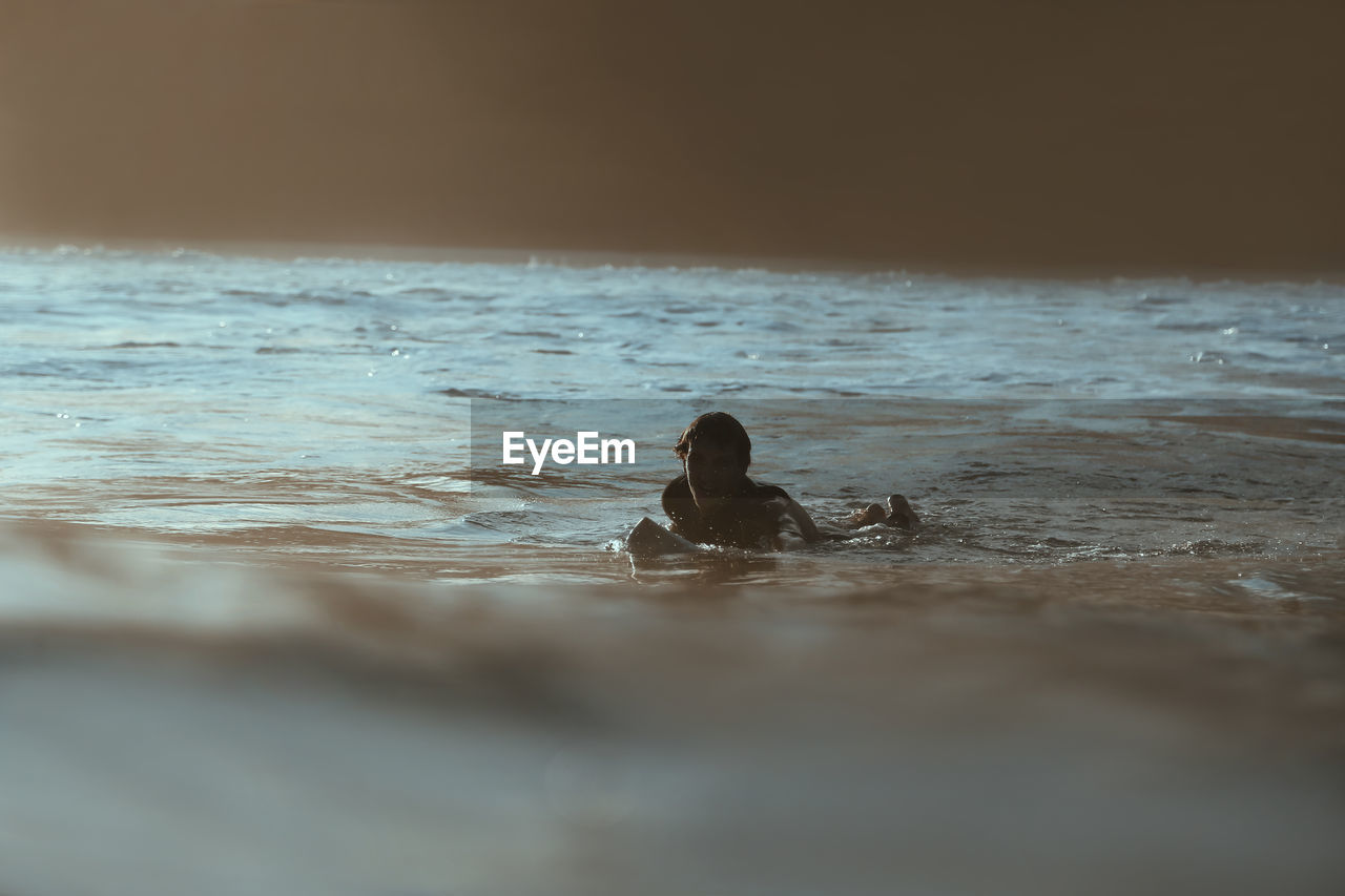 Surfer lying on surfboard at sunset