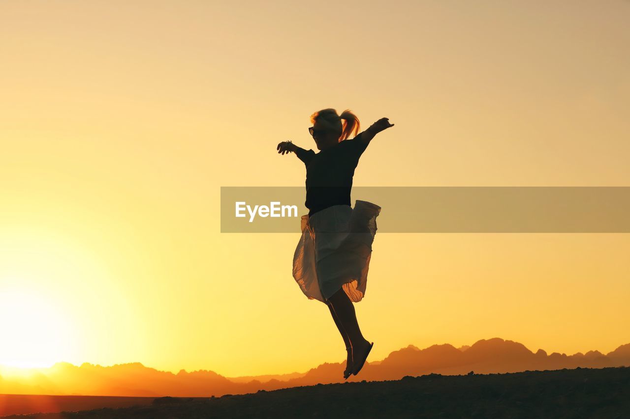 Full length of silhouette woman jumping against clear orange sky