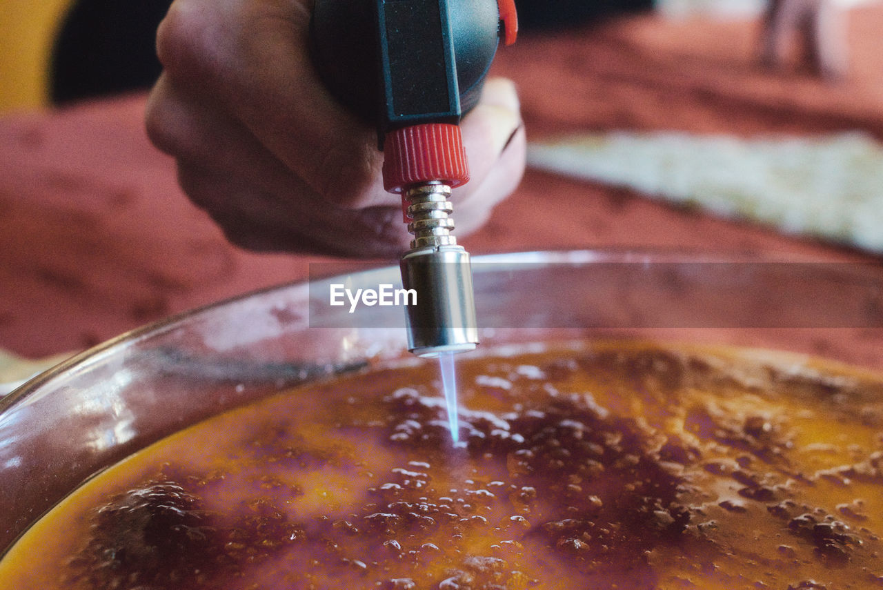 Close-up of hand preparing creme brulee with burner