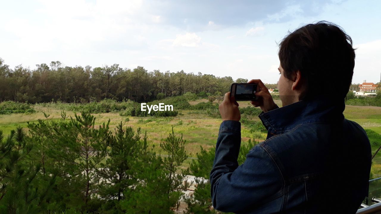 Man photographing with mobile phone against trees